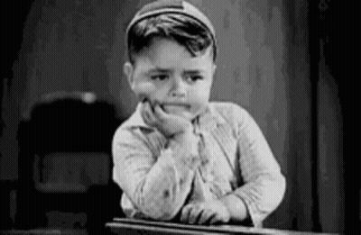 A Black And White Photo Of A Young Boy Sitting At A Desk With His Hand On His Face . GIF