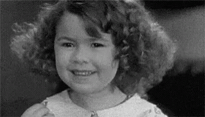 A Black And White Photo Of A Young Girl With Curly Hair Smiling . GIF