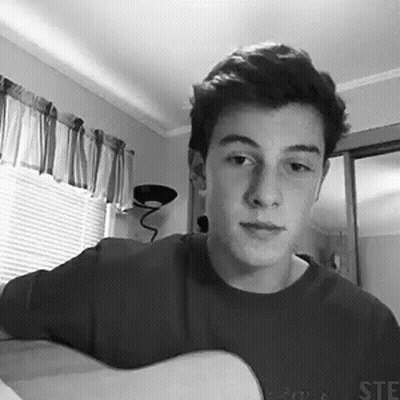 A Black And White Photo Of A Young Man Holding A Guitar In A Room . GIF