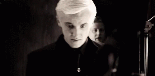 A Black And White Photo Of A Young Man In A Black Suit And Tie . GIF