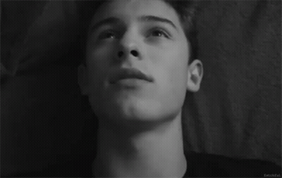 A Black And White Photo Of A Young Man Laying On A Bed Looking Up At The Sky . GIF