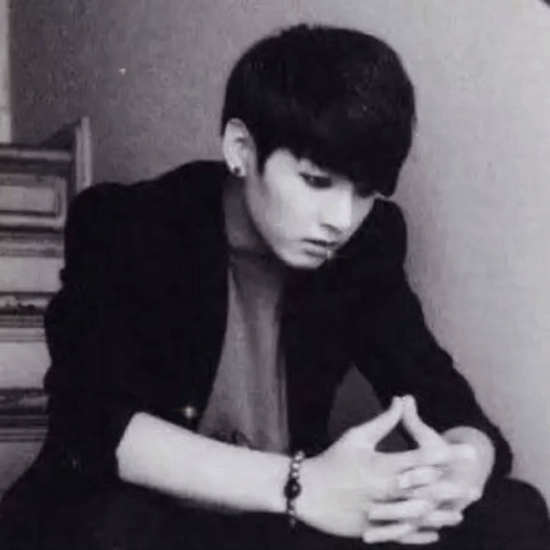 A Black And White Photo Of A Young Man Sitting Down With His Hands Folded And A Bracelet On His Wrist . GIF