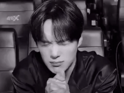 A Black And White Photo Of A Young Man Sitting In A Theater With His Eyes Closed And His Hands Folded . GIF
