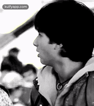 A Black And White Photo Of A Young Man Talking To Someone In A Crowd . GIF