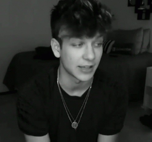 A Black And White Photo Of A Young Man Wearing A Necklace That Has The Letter M On It GIF