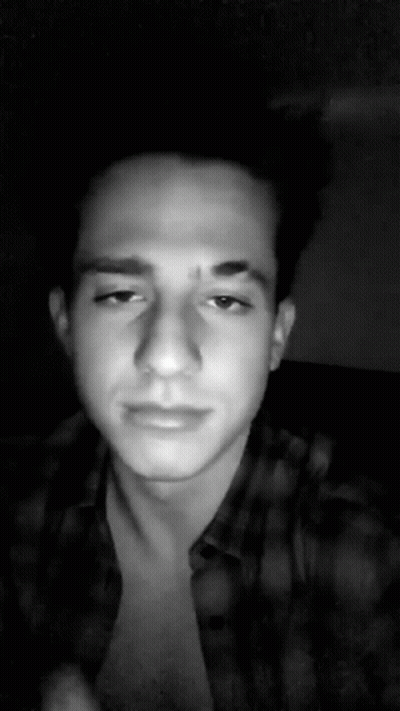 A Black And White Photo Of A Young Man Wearing A Plaid Shirt And Looking At The Camera . GIF