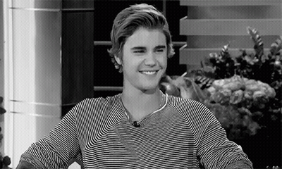 A Black And White Photo Of A Young Man Wearing A Striped Shirt Smiling . GIF