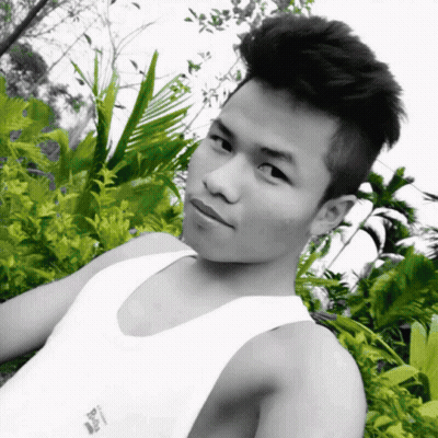 A Black And White Photo Of A Young Man Wearing A White Tank Top With A Few Plants Behind Him GIF