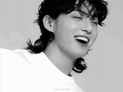 A Black And White Photo Of A Young Man With A Ponytail Smiling GIF