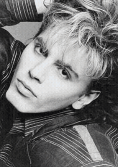 A Black And White Photo Of A Young Man With Curly Hair And A Striped Shirt . GIF