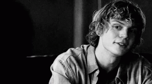 A Black And White Photo Of A Young Man With Curly Hair Sitting At A Table . GIF