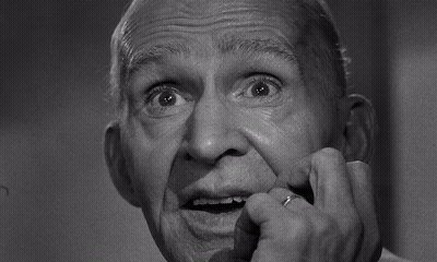 A Black And White Photo Of An Older Man With His Hand On His Mouth GIF