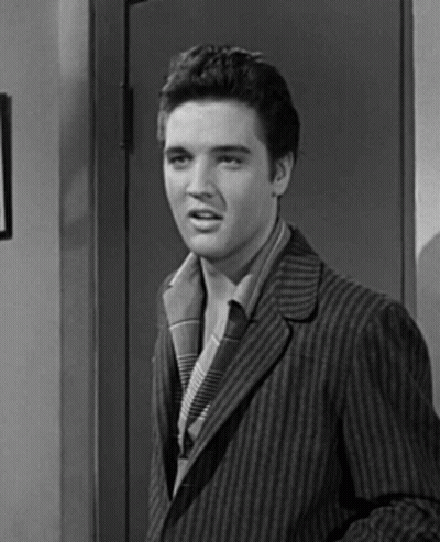 A Black And White Photo Of Elvis Presley In A Striped Suit Standing In Front Of A Door . GIF