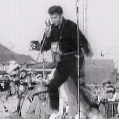 A Black And White Photo Of Elvis Presley Playing A Guitar And Singing Into A Microphone On A Stage . GIF