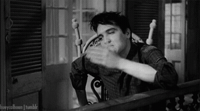 A Black And White Photo Of Elvis Presley Sitting In A Rocking Chair And Waving His Hand . GIF
