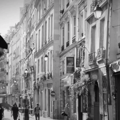 A Black And White Photo Of People Walking Down A Narrow Street With A Sign That Says Hotel Voyageur On It GIF