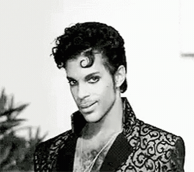 A Black And White Photo Of Prince In A Suit And Necklace . GIF
