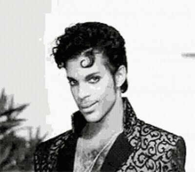 A Black And White Photo Of Prince Wearing A Suit Jacket And Necklace . GIF