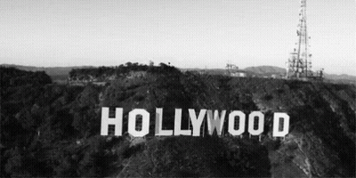 A Black And White Photo Of The Hollywood Sign Sitting On Top Of A Hill Surrounded By Trees . GIF