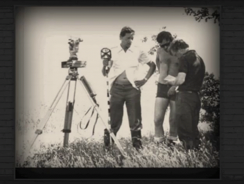 A Black And White Photo Of Three Men Standing In A Field With A Camera On A Tripod GIF