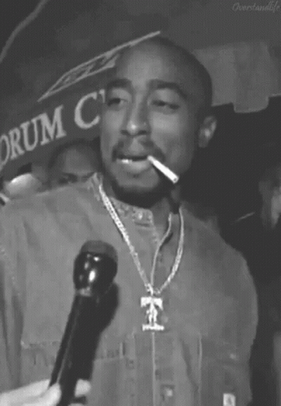 A Black And White Photo Of Tupac Shakur Smoking A Cigarette While Holding A Microphone . GIF