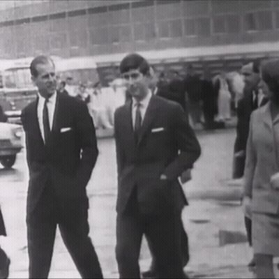 A Black And White Photo Of Two Men In Suits Standing Next To Each Other On A Street . GIF