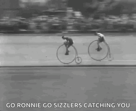 A Black And White Photo Of Two Men Riding Bicycles On A Road . GIF