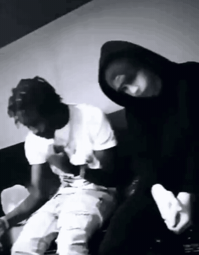 A Black And White Photo Of Two Men Sitting On A Couch . One Of The Men Is Wearing A Mask . GIF