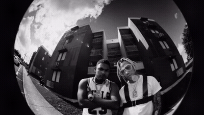 A Black And White Photo Of Two Men Standing In Front Of A Building With One Wearing A Number 25 Jersey GIF