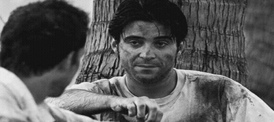 A Black And White Photo Of Two Men Talking To Each Other . One Of The Men Is Holding A Knife . GIF