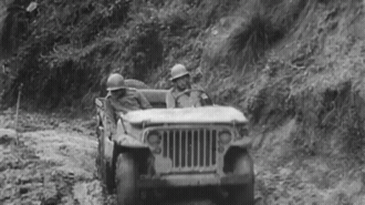 A Black And White Photo Of Two Soldiers Driving A Jeep Down A Dirt Road . GIF