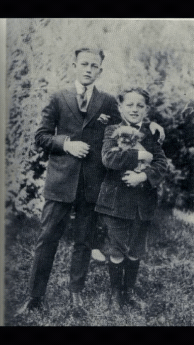 A Black And White Photo Of Two Young Boys Holding A Dog GIF