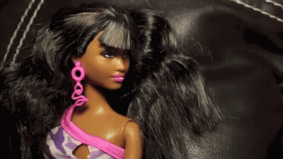 A Black Barbie Doll Wearing Pink Earrings And A Purple Top GIF