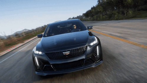 A Black Cadillac Is Driving Down A Road With Mountains In The Background GIF