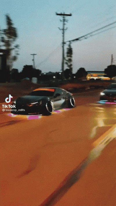 A Black Car Is Driving Down A Dirt Road With A School Bus In The Background .. GIF