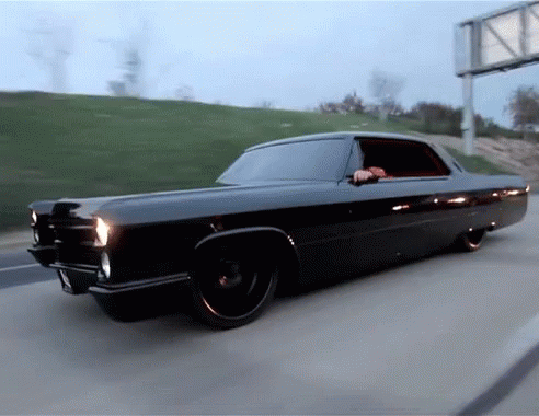 A Black Car Is Driving Down A Highway With A Billboard In The Background GIF