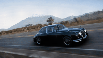 A Black Car Is Driving Down A Road In Front Of Mountains GIF