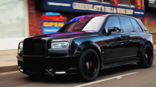 A Black Car Is Driving Down A Street In Front Of A Store That Says ' Chen 'S ' On It GIF
