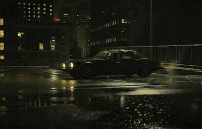 A Black Car Is Driving On A Wet Street At Night . GIF