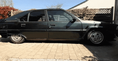A Black Car Is Parked In A Driveway With A Fence In The Background GIF