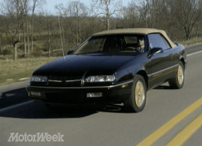 A Black Car With A Tan Top Is Driving Down A Road With Motorweek Written On The Bottom GIF