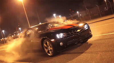 A Black Car With An Orange Stripe On The Side Is Driving Down A Street At Night GIF