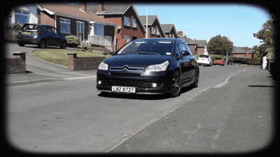 A Black Car With License Plate Lnz 8727 Is Driving Down A Street GIF