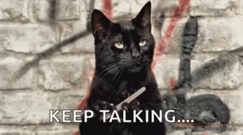 A Black Cat Is Holding A Pair Of Scissors In Front Of A Brick Wall . GIF