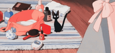 A Black Cat Is Sitting On A Striped Rug Next To A Bag Filled With Cosmetics . GIF