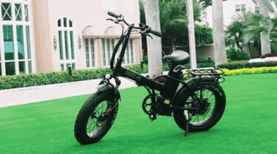 A Black Folding Electric Bike Is Parked On A Lush Green Field . GIF