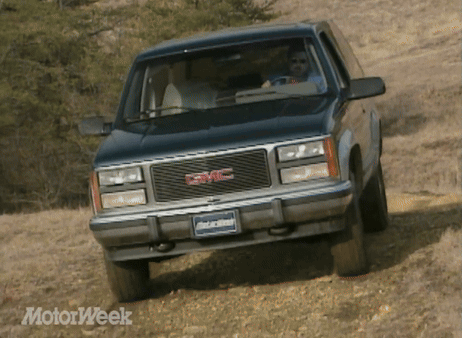 A Black Gmc Truck Is Driving Down A Dirt Road GIF