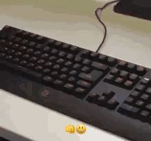 A Black Keyboard Is Sitting On Top Of A White Table Next To Two Smiley Faces . GIF