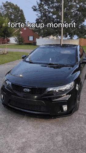 A Black Kia Car Is Parked In A Driveway With The Words Forte Koup Moment Above It GIF
