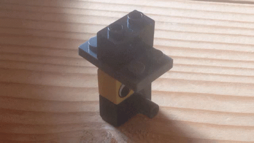 A Black Lego Block Is Sitting On Top Of A Wooden Surface GIF